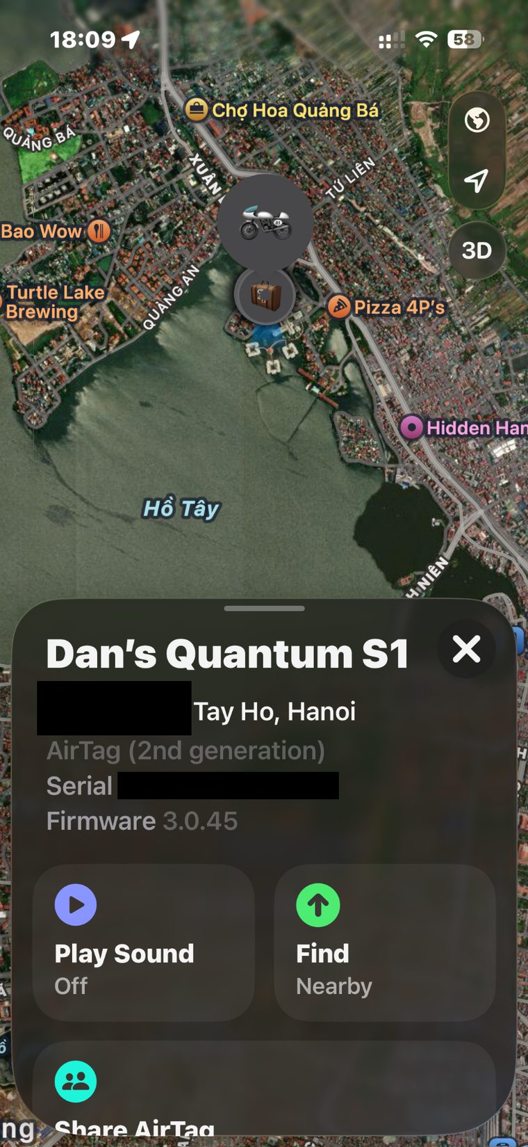 An iPhone Find My screen. A dark satellite map of West Lake in Hanoi with amber map labels, a motorbike icon and a luggage icon at a single pin. A panel below reads 'Dan's Quantum S1', then a solid black redaction box followed by 'Tay Ho, Hanoi', then 'AirTag (2nd generation)', 'Serial' with a second solid black redaction box, and 'Firmware 3.0.45'.